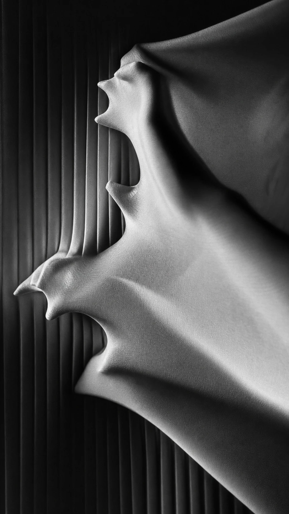 A monochrome close-up of stretched fabric pulled into spiky, organic peaks against a vertically ribbed dark backdrop.