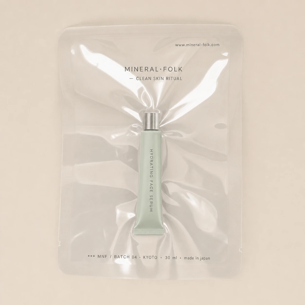 A minimalist flat-lay product shot of a sage-green skincare serum tube sealed inside a transparent vacuum pouch on a neutral beige backdrop.