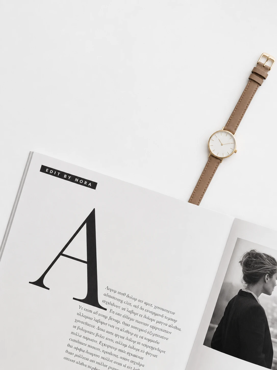 A minimalist flat-lay of an open editorial magazine spread beside an elegant women's wristwatch on a clean white surface.