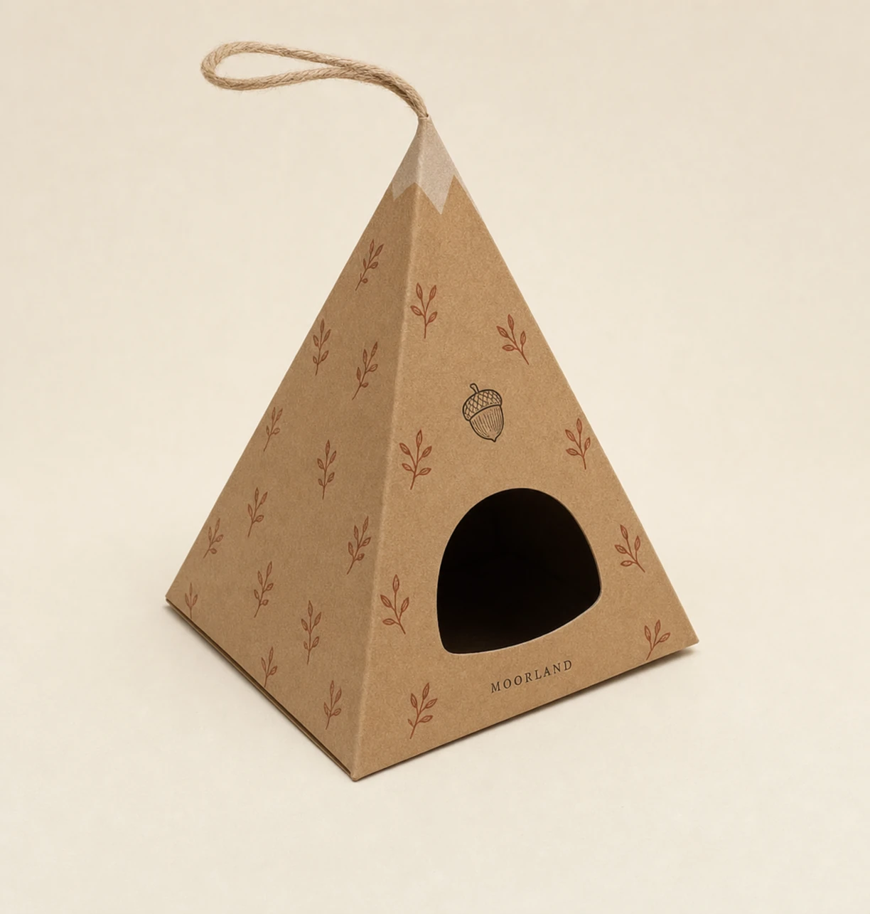A pyramid-shaped kraft paper gift box with a twine handle, botanical print, and a die-cut window, photographed against a soft neutral backdrop.