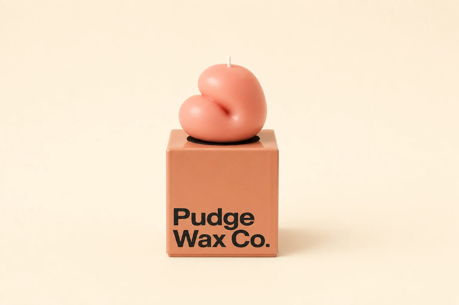 A minimalist product photograph of a blobby, organic-shaped candle sitting atop a cube package box against a soft cream backdrop.