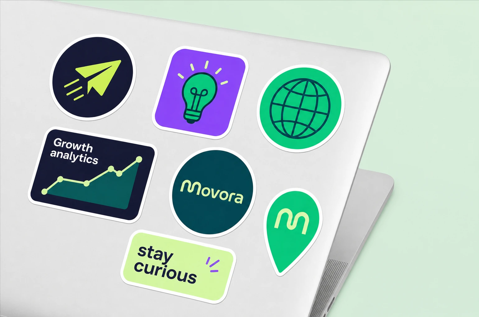 A photorealistic mockup of a laptop lid decorated with a cluster of die-cut branded stickers in green, purple, and dark navy.