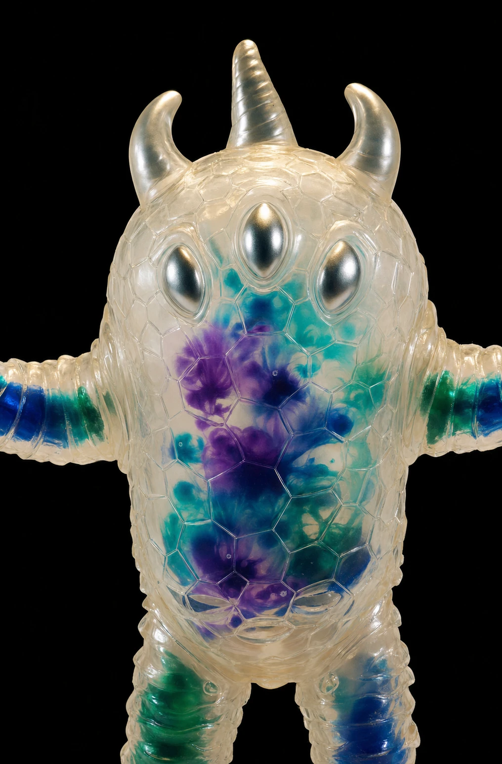 A translucent vinyl designer toy of a three-eyed horned monster with watercolor-like internal color bleeds, shot against pure black.