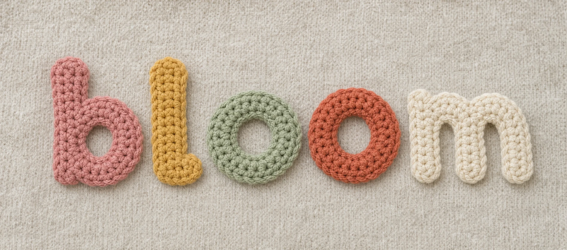 The word 'bloom' spelled out in handmade crocheted lowercase letters resting on a knitted fabric background.