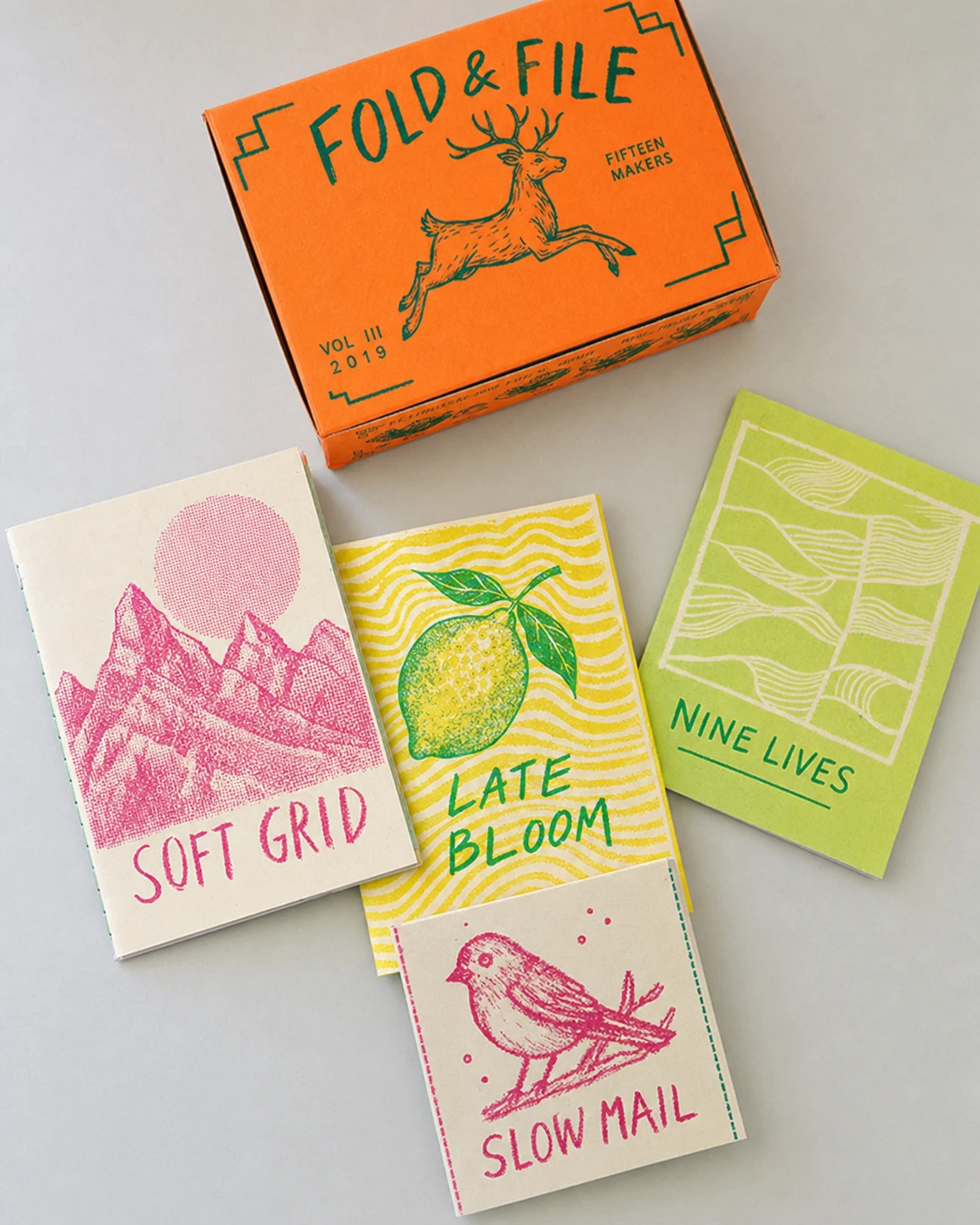 A flat-lay product photo of a riso-printed zine collection with a branded box and four illustrated booklet covers in vivid fluorescent inks.