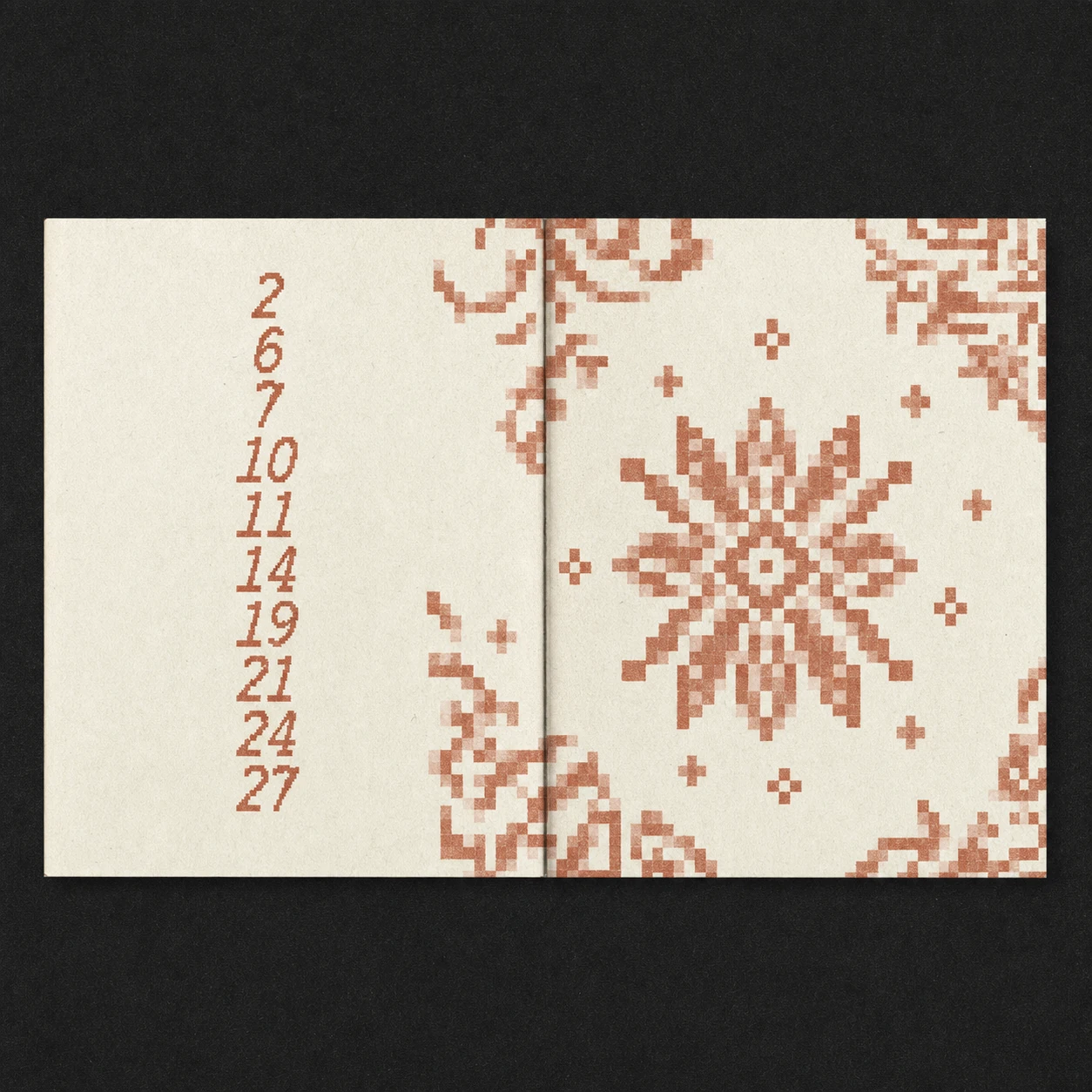 An open booklet spread photographed flat on dark paper, featuring a pixelated cross-stitch-style snowflake motif and a vertical column of numbers in warm terrac