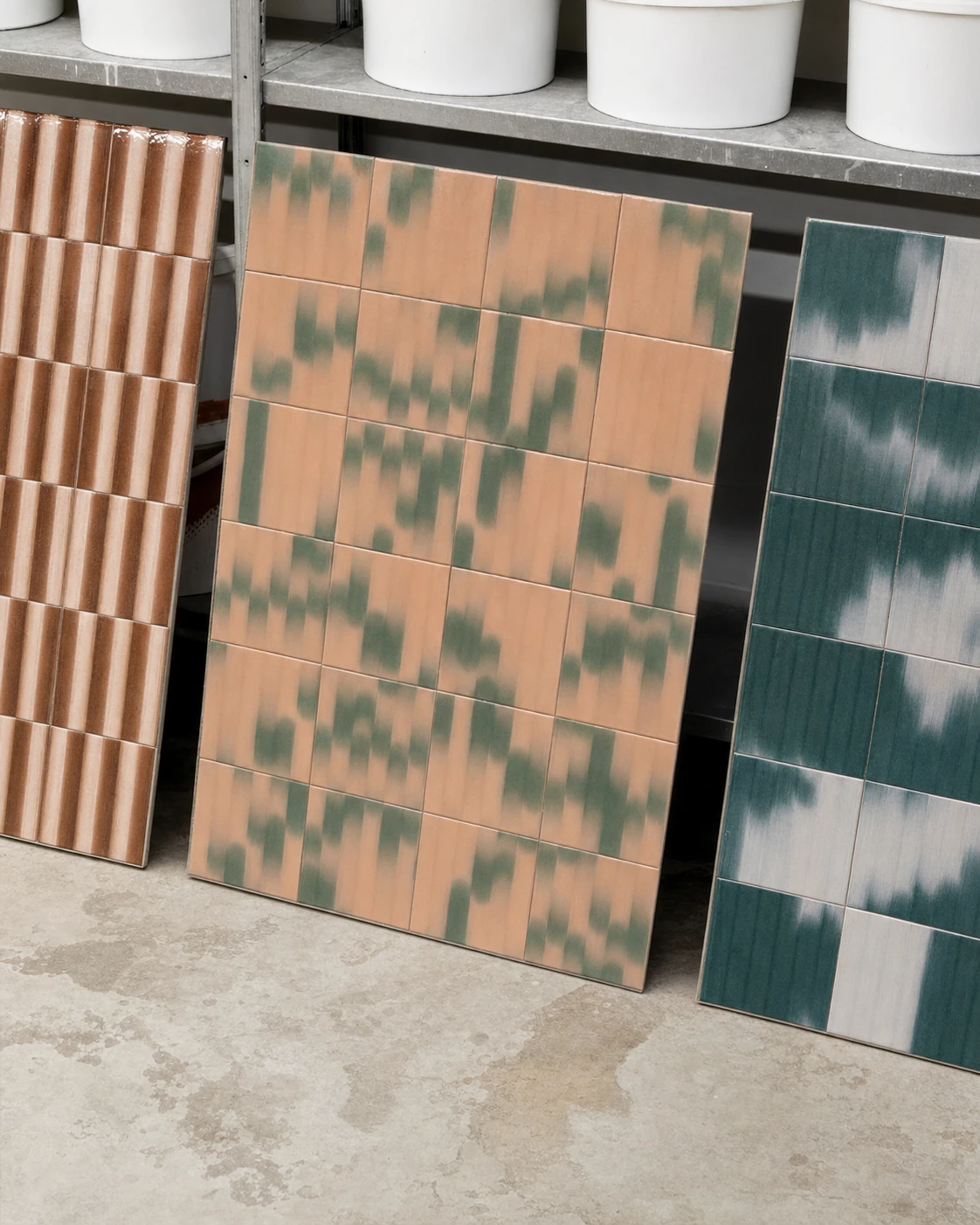 An editorial product photograph of three decorative ceramic tile panels leaning against a shelf in an artisanal studio setting.