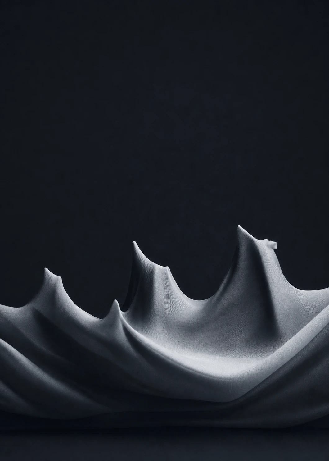 A moody studio photograph of pale draped fabric pulled into sharp peaks resembling a mountain range or wave crests against deep darkness.
