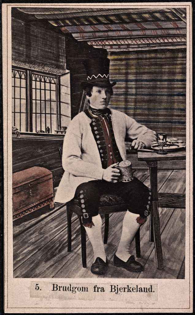 Vintage photograph of a man in traditional Norwegian attire seated at a table in a rustic cabin.