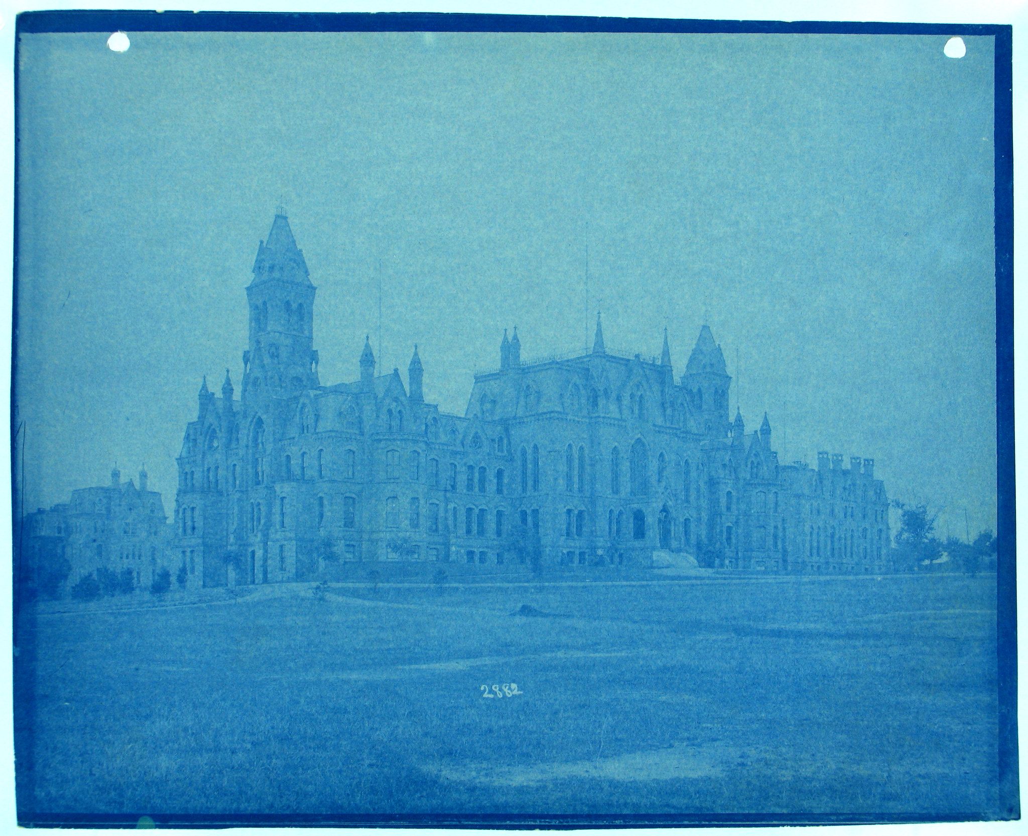 Cyanotype photograph of a grand, ornate building with multiple towers and spires, set against a pale blue sky.