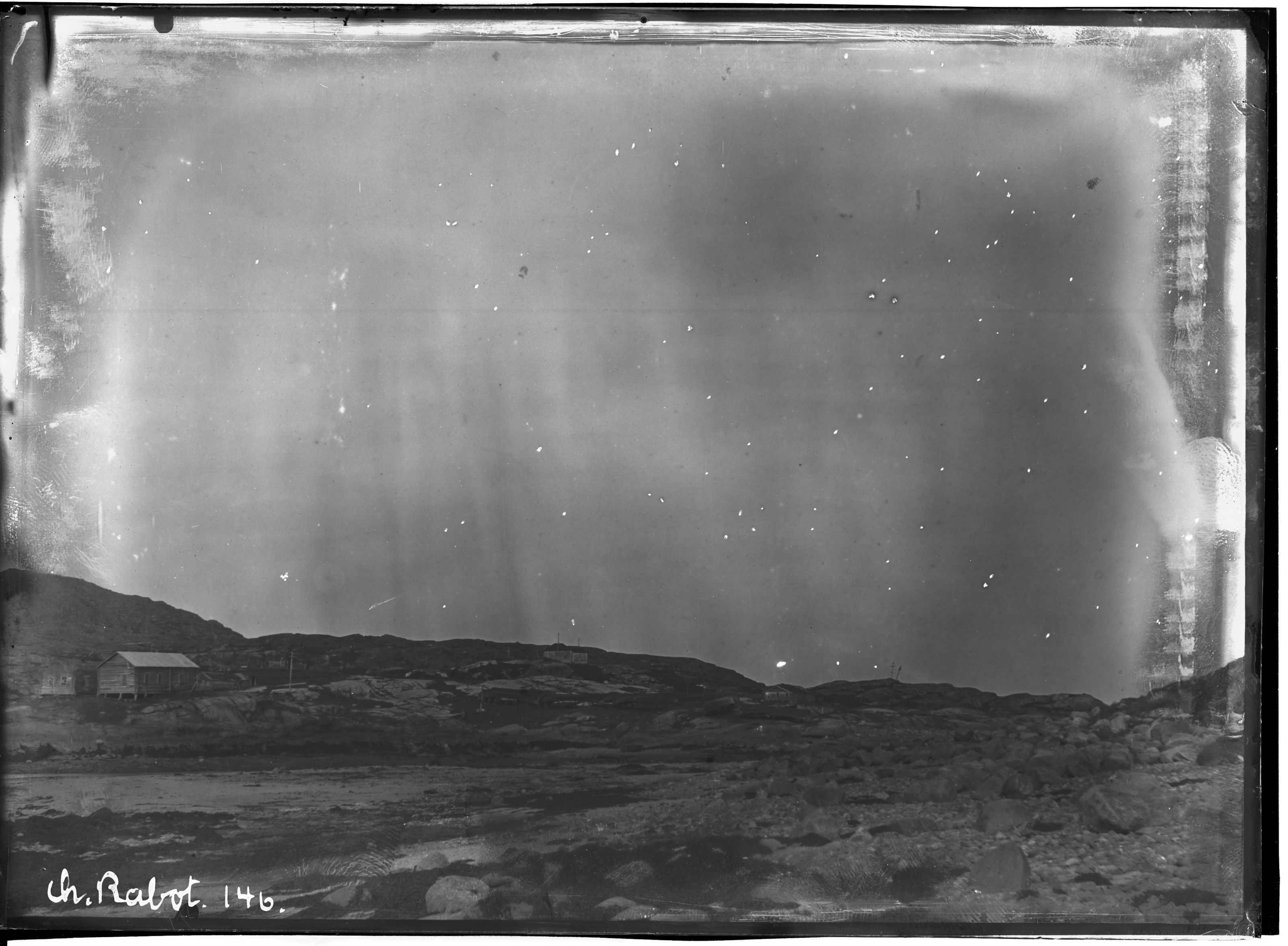 A vintage black and white photograph of a landscape under a night sky with stars and a small building.