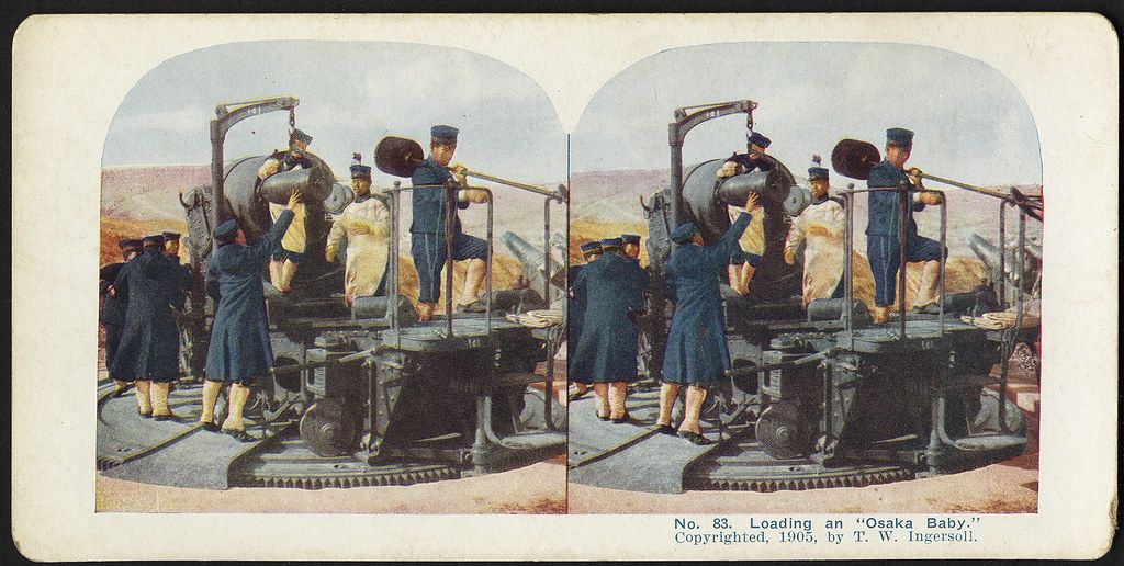Stereoscopic photograph from 1905 titled "Loading an 'Osaka Baby'" showing men in uniform loading a large machine onto a wagon on railroad tracks.
