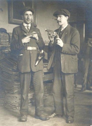 A vintage black and white photograph of two men in early 20th-century attire posing with firearms.
