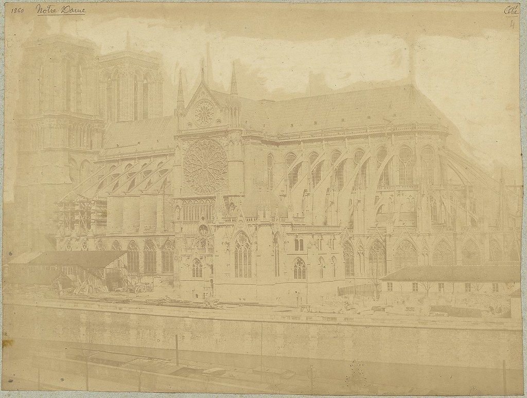 A sepia-toned vintage photograph of Notre Dame Cathedral in Paris, dated 1860, showcasing its Gothic architecture and a bustling street scene.