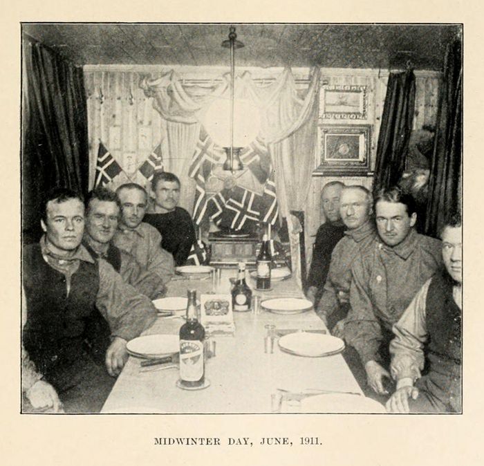 A black and white photograph of a group of men seated around a long table, celebrating Midwinter Day in June 1911.