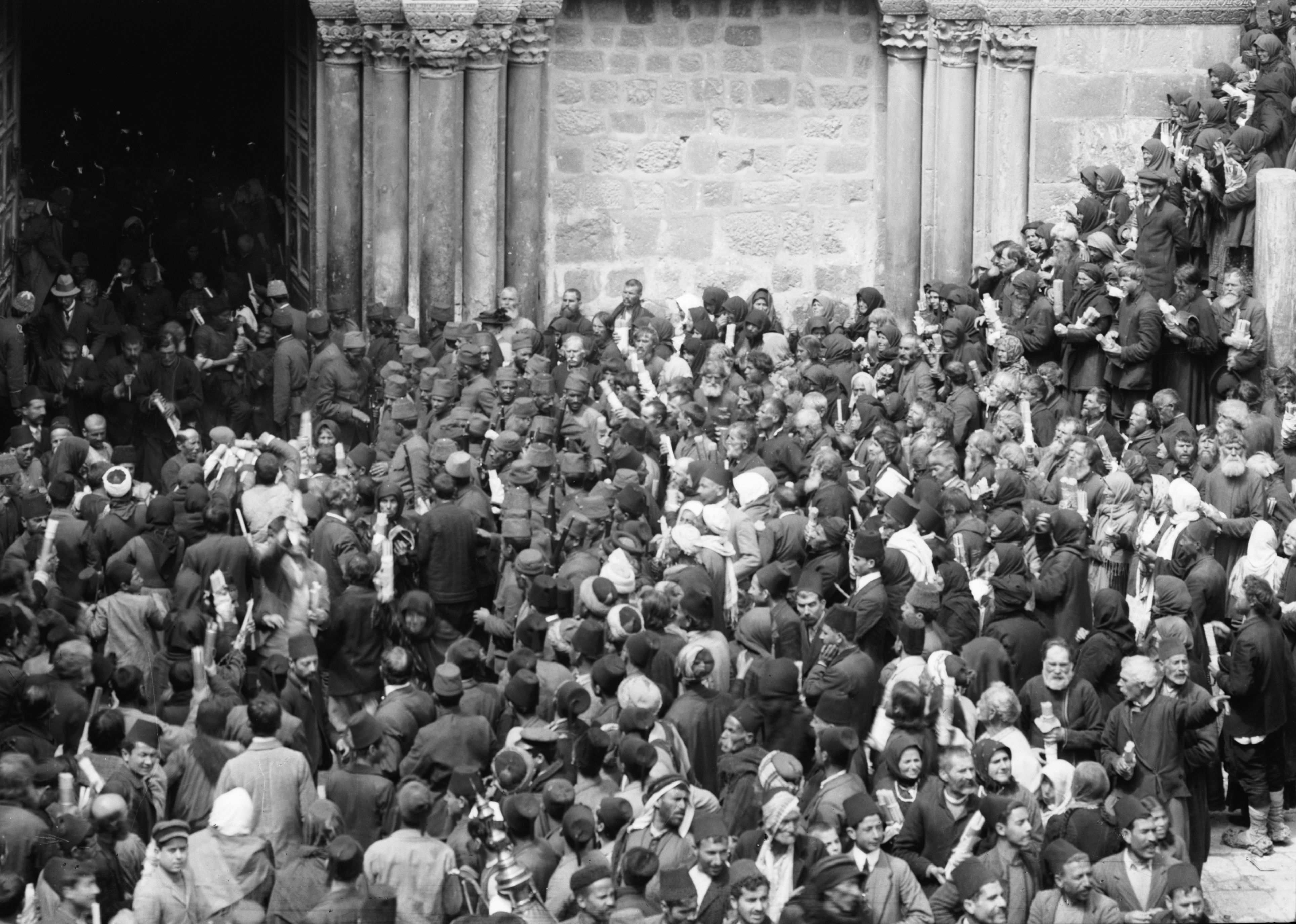 A black and white photograph of a large crowd of people gathered in front of a building with columns.