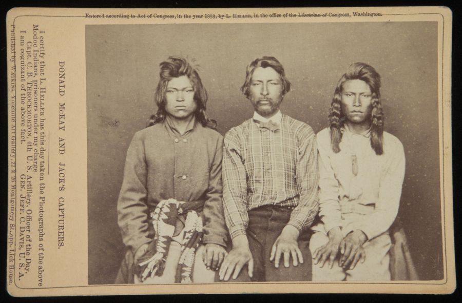 A sepia-toned photograph from 1868, featuring three Native American men standing shoulder to shoulder, looking directly at the camera.