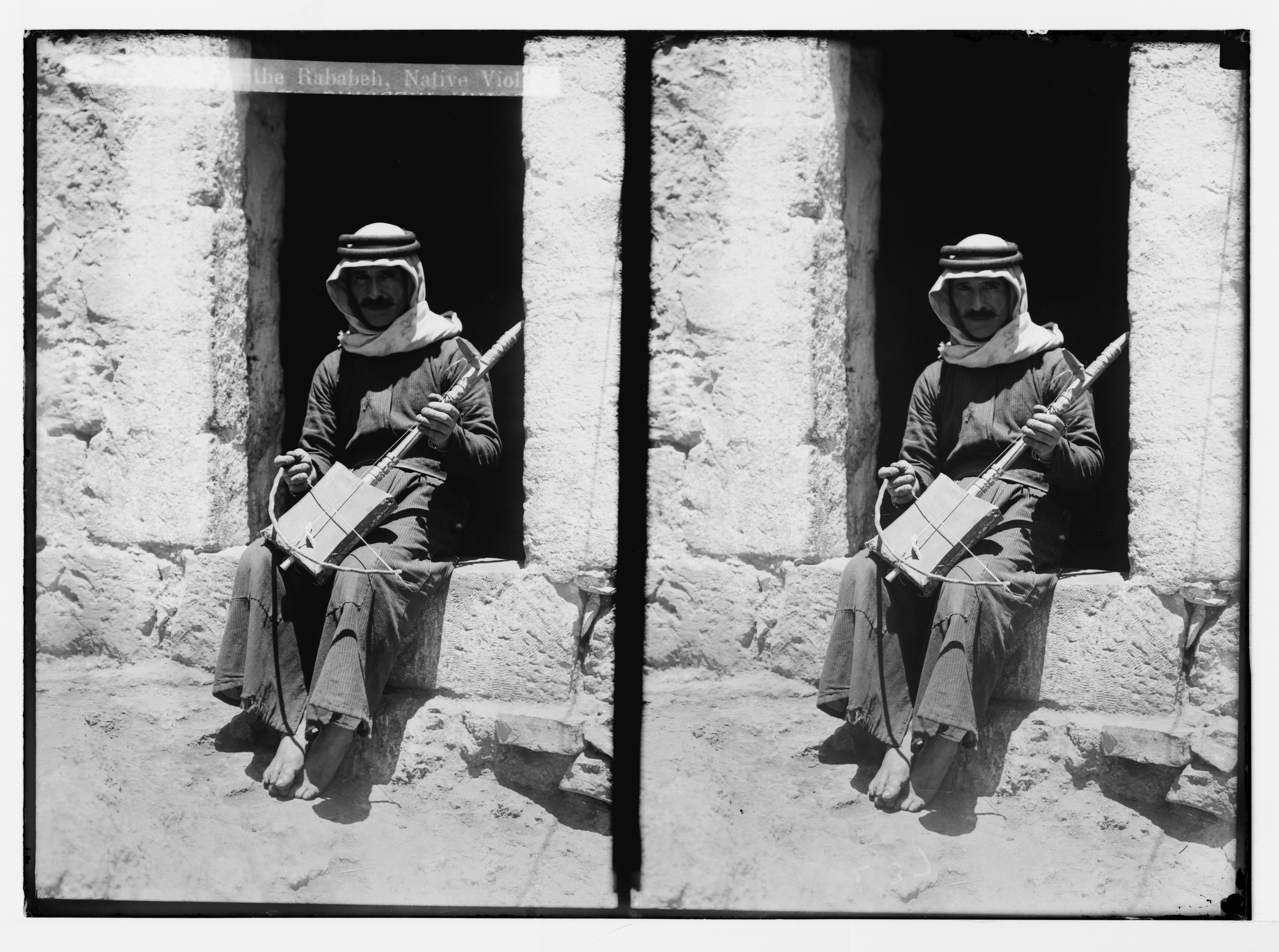 Stereoscopic photograph of a man playing a long-necked lute-like instrument while seated in a window opening.