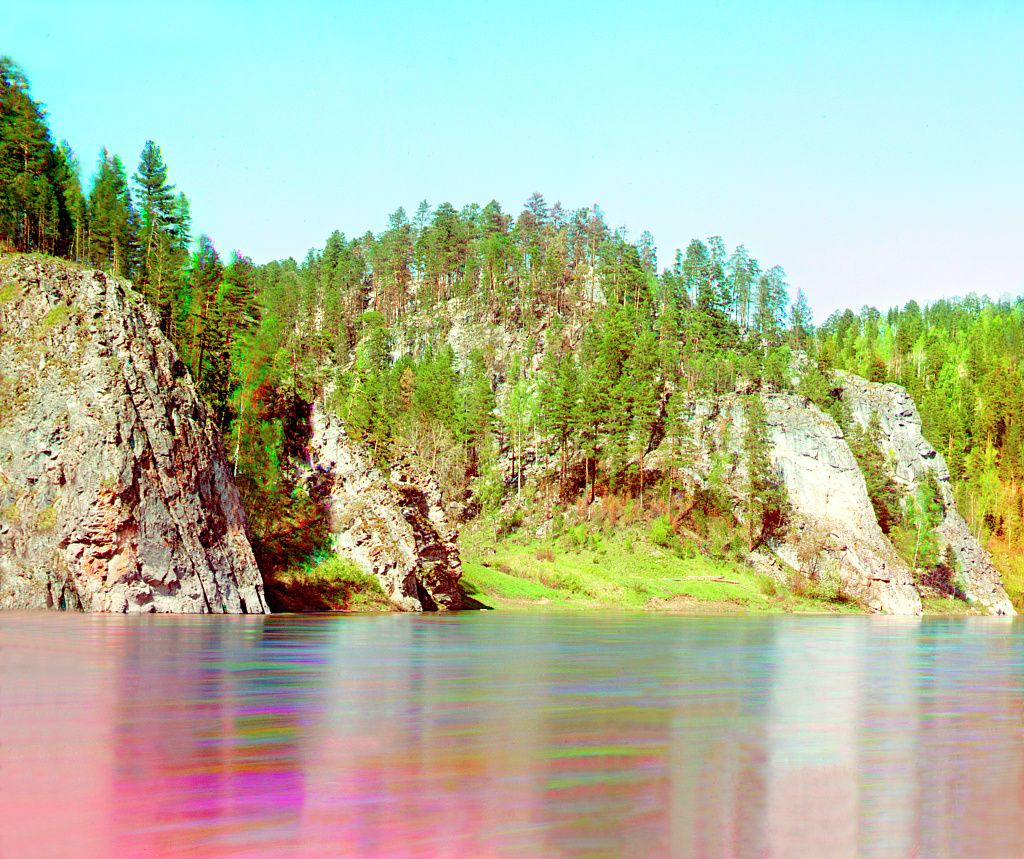 A scenic view of a river flowing alongside a rocky cliff covered in lush green forest.