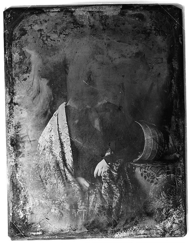A vintage daguerreotype portrait of a person wearing a patterned dress and a large hat, with their face obscured by shadow.