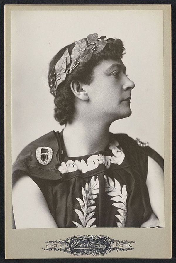 A vintage black and white photograph of a person in a theatrical or historical costume.