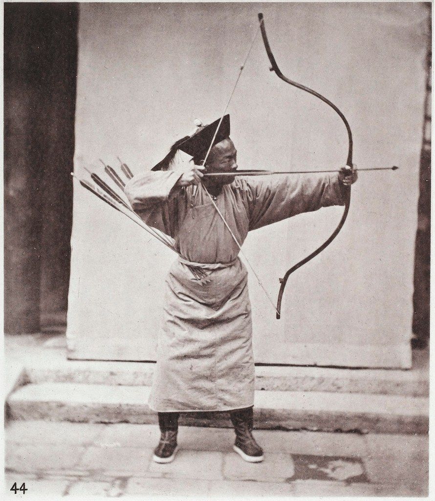 Vintage black and white photograph of a man in traditional clothing practicing archery.