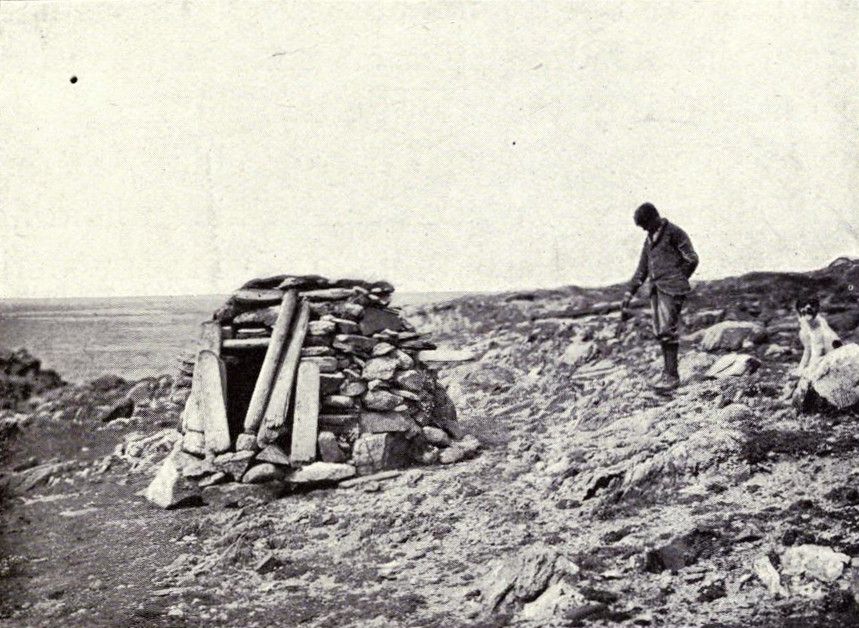 A vintage black and white photograph of a stone structure and a man in a rugged landscape.