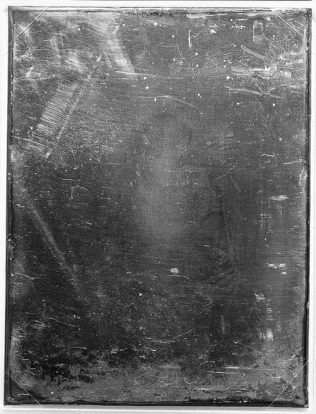 A black and white photograph of a heavily distressed surface covered in scratches, smudges, and dust particles.