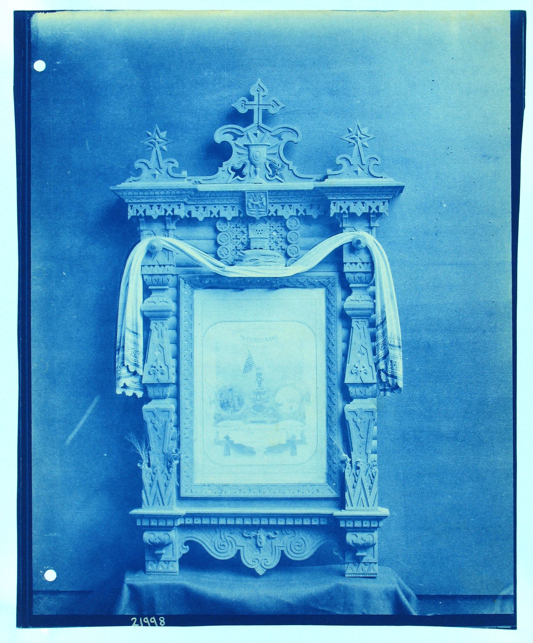A cyanotype photograph of an ornate altar or religious frame with intricate carvings and a faded religious scene within the frame.