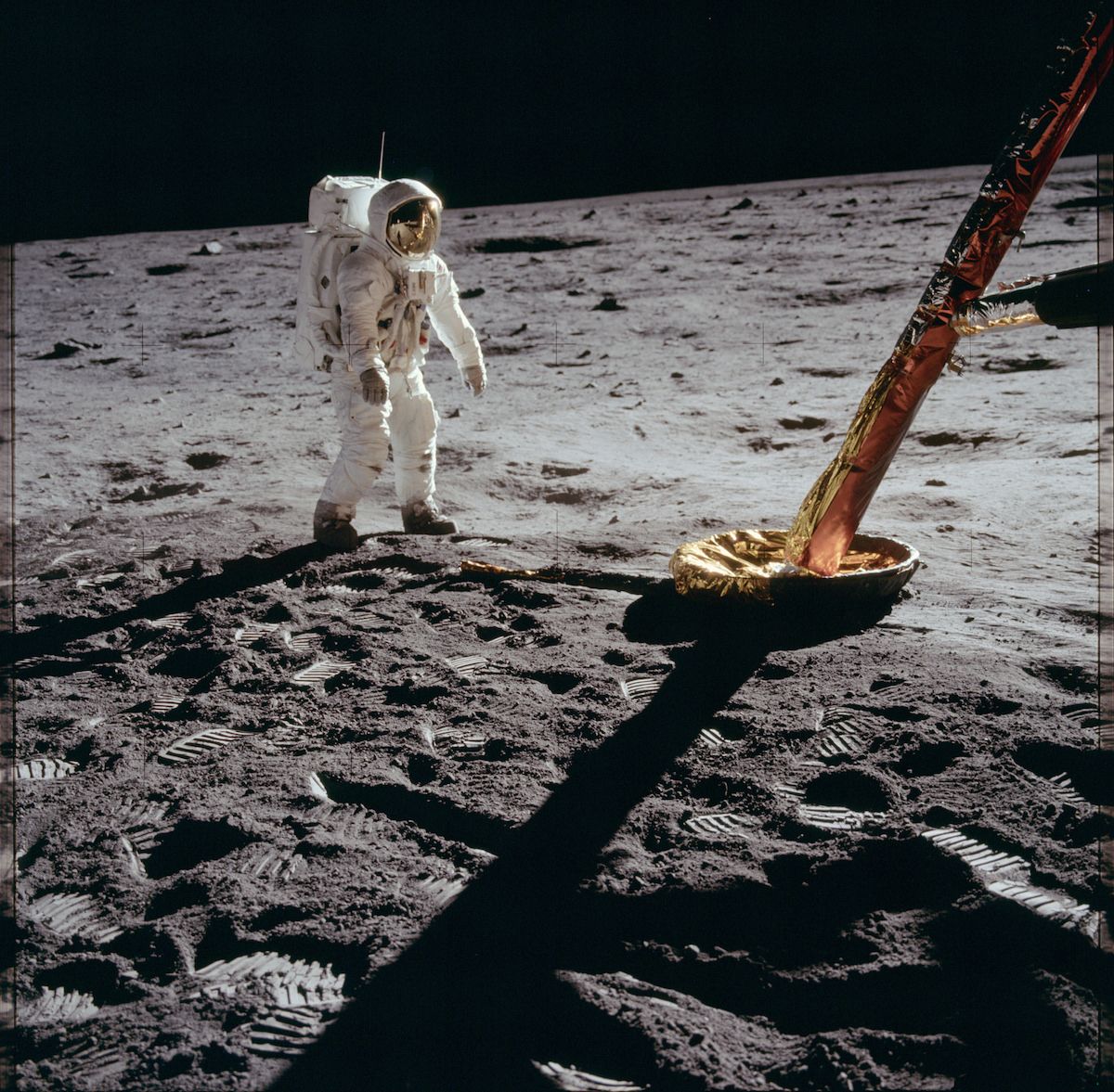 An astronaut walks on the moon, leaving footprints in the gray dust. The lunar module is visible in the background, casting a long shadow.