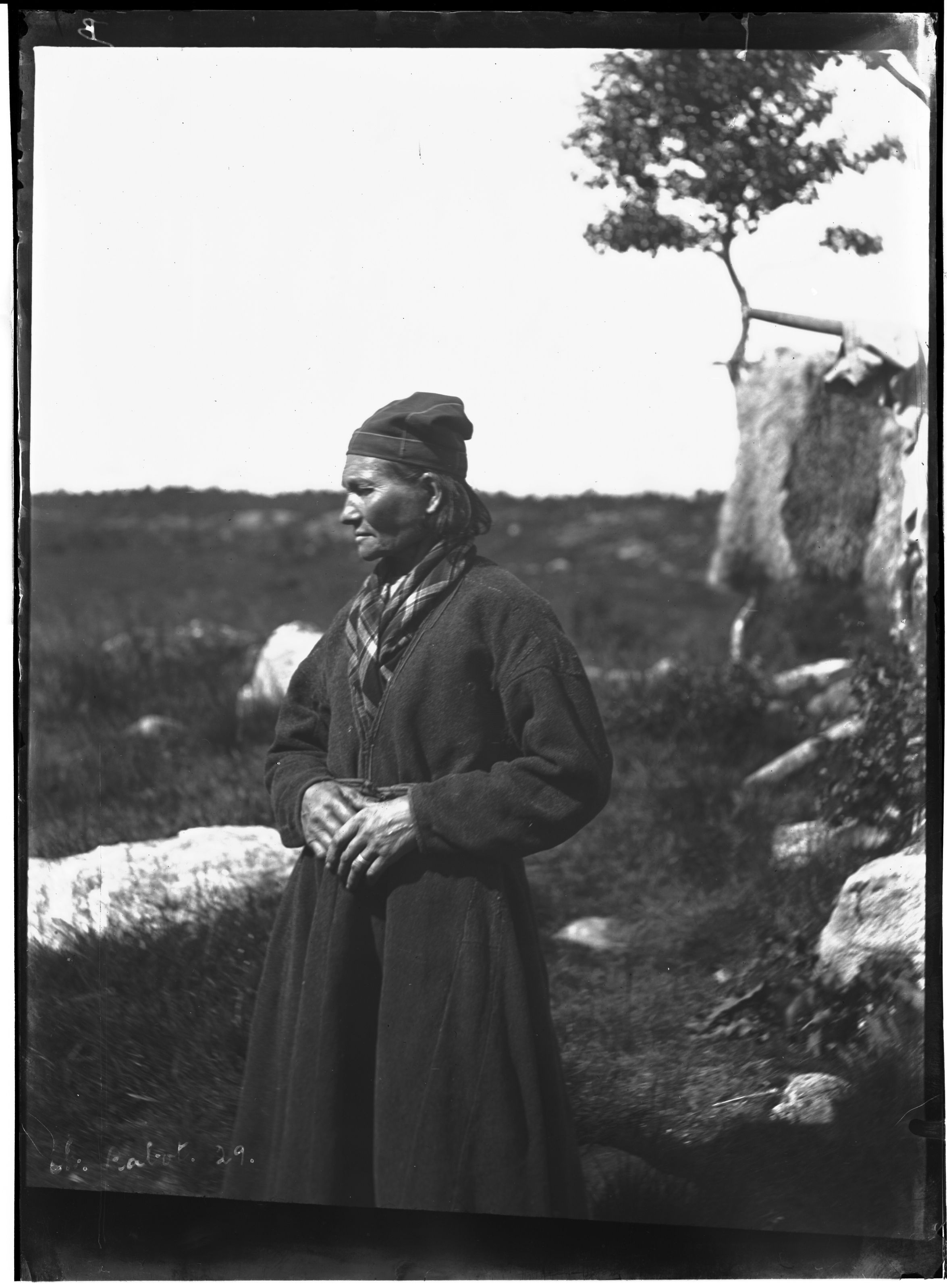 Vintage black and white photograph of a man in traditional clothing standing in a rocky landscape.