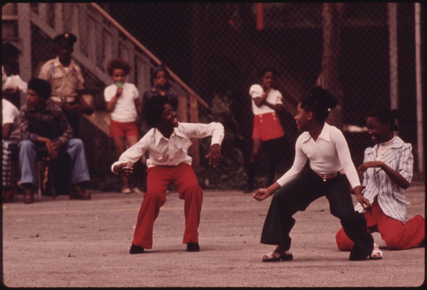 Two young boys dancing in a street, with a crowd of people watching in the background.