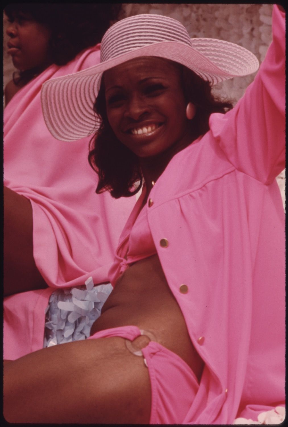 A smiling Black woman wearing a pink outfit and a straw hat.