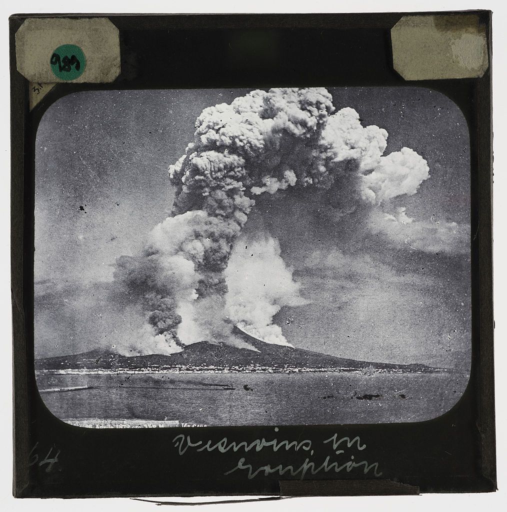 A black and white photograph of Mount Vesuvius erupting, with a large plume of smoke and ash rising into the sky.