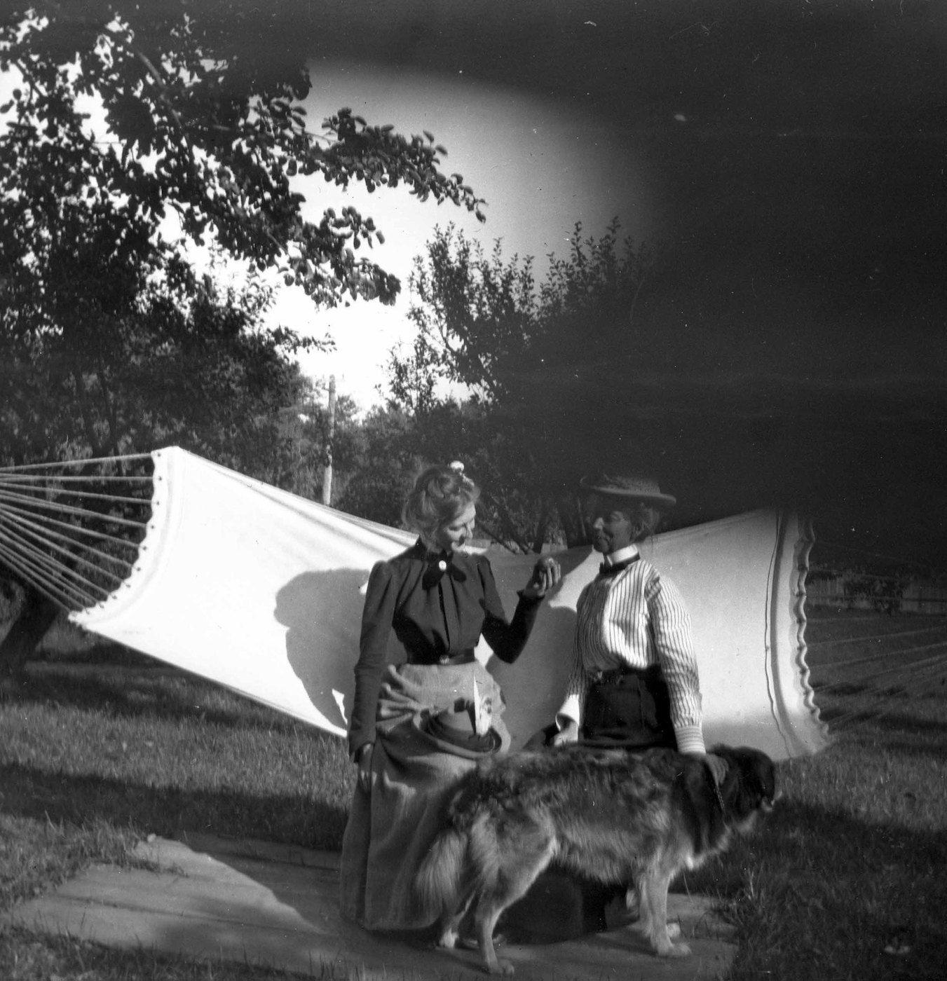 Vintage black and white photograph of two women and a dog in a garden setting.
