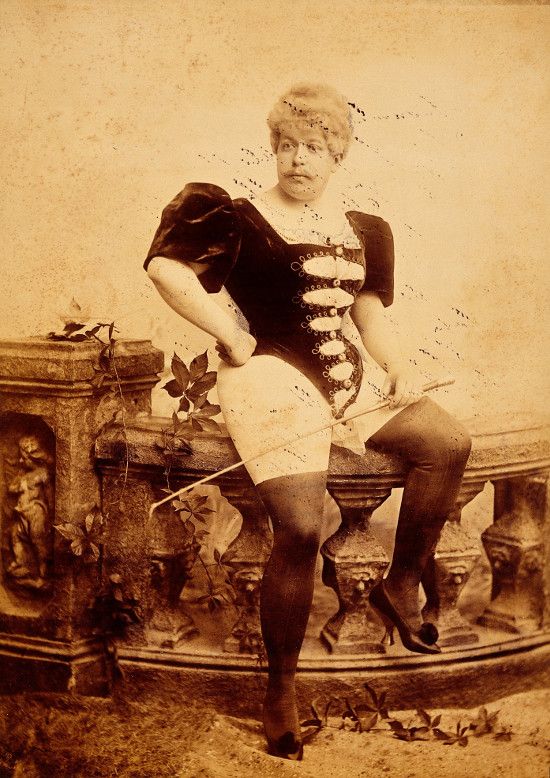 A vintage sepia-toned photograph of a woman in a unique outfit posing on a stone balustrade.