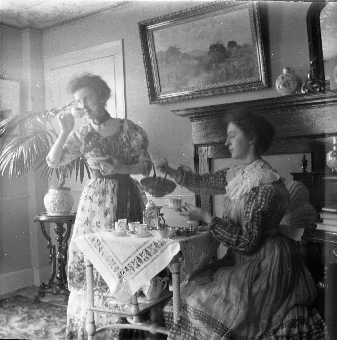 A black and white photograph of two women having tea in a well-furnished room.