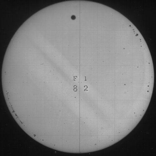A circular view through a telescope with a dark dot near the top center, a grid pattern, and text 'F1' above '82'.