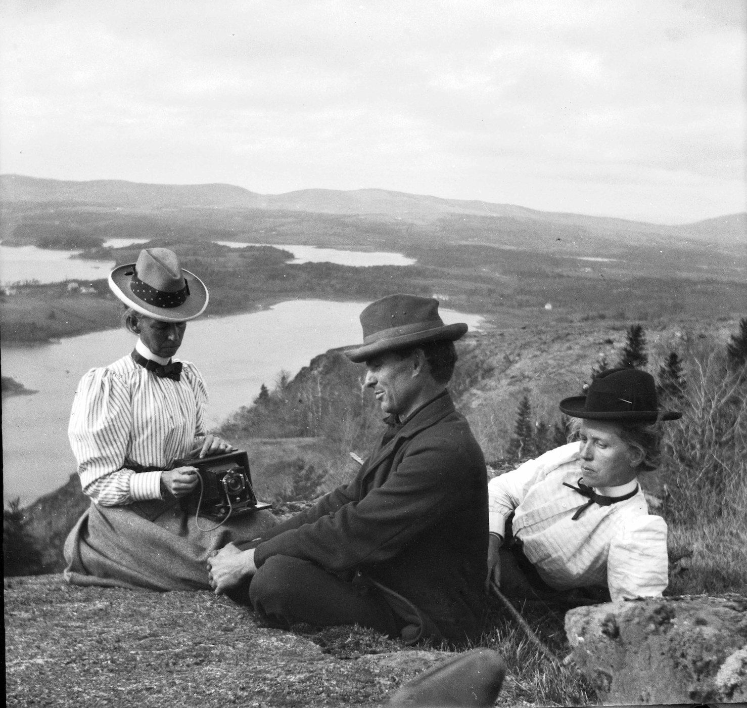 A vintage black and white photograph of three people in a scenic landscape.