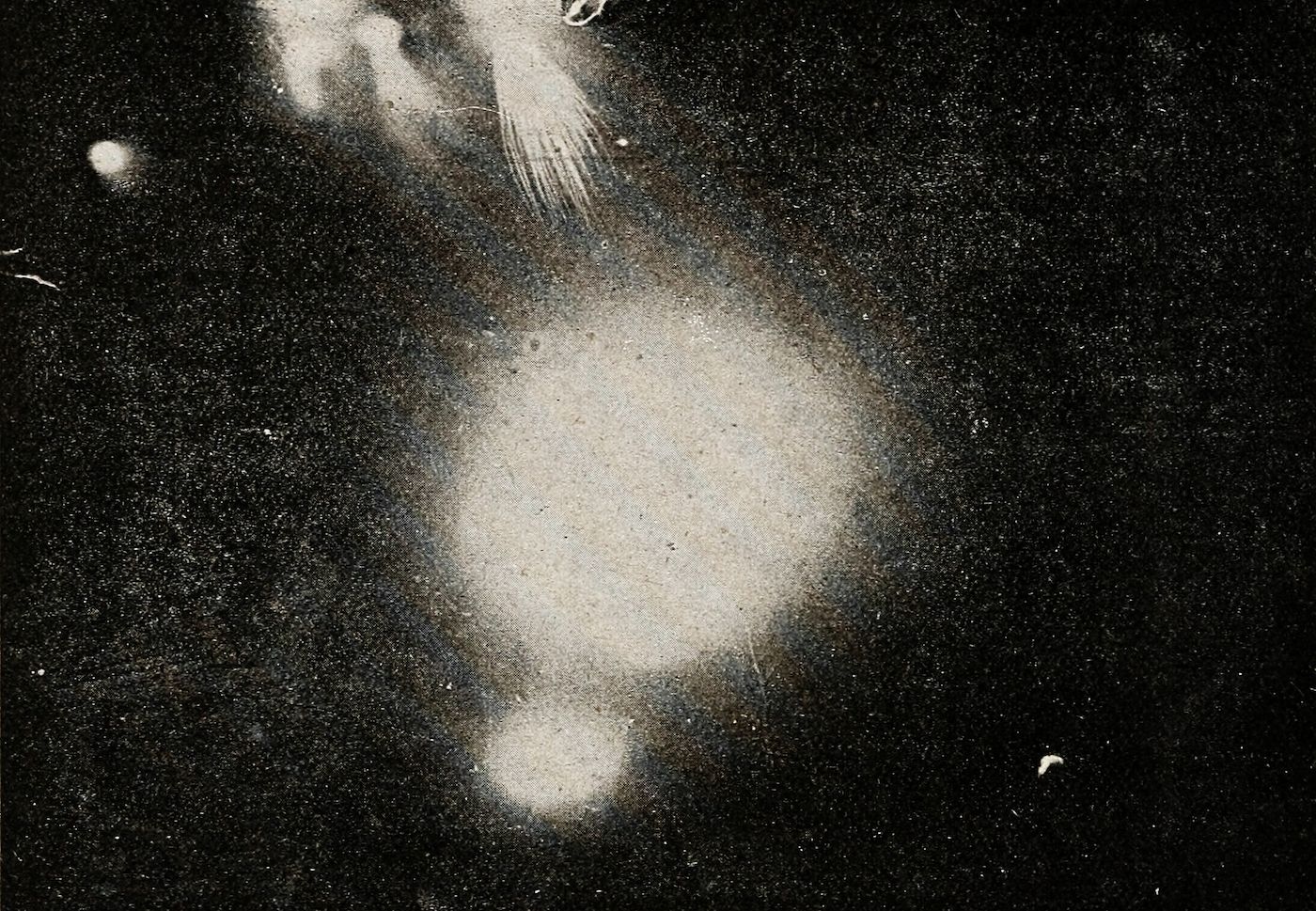 Vintage black and white photograph of a spiral galaxy with a bright central bulge and faint spiral arms, surrounded by numerous stars.