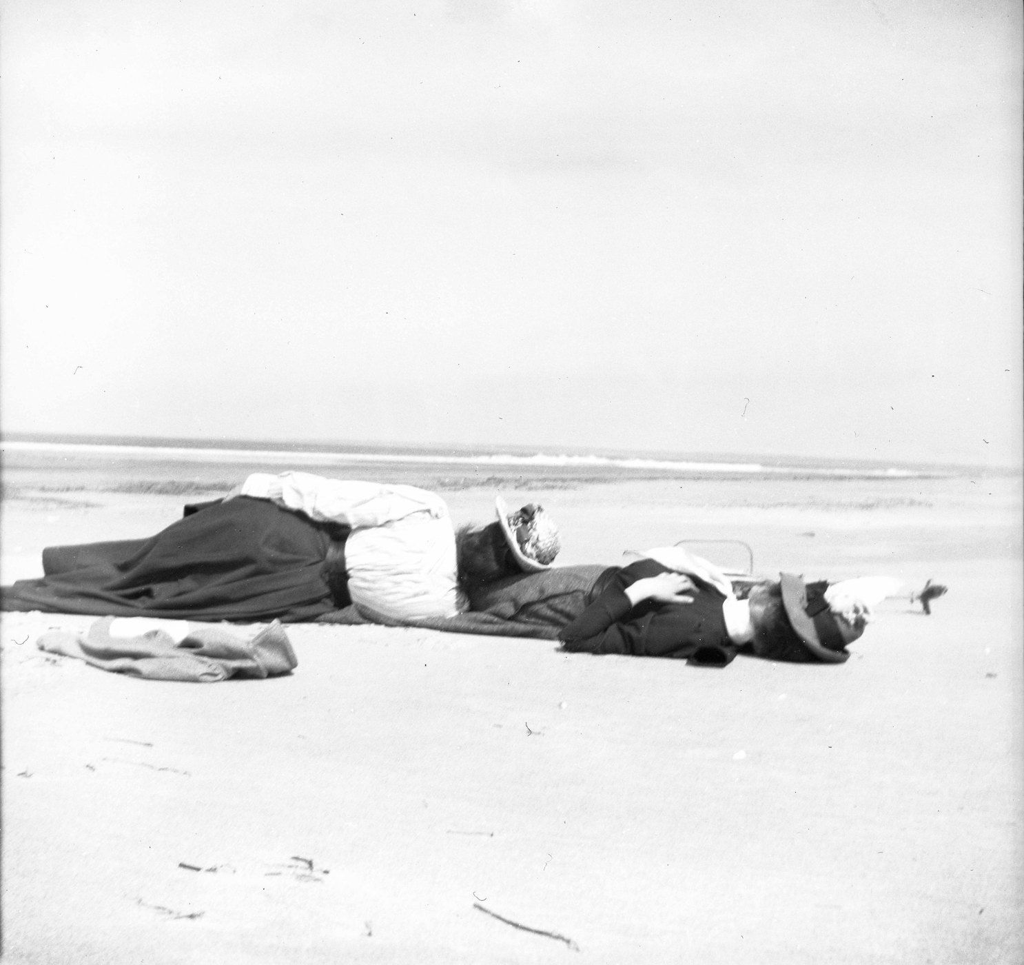 A black and white photograph of two people lying on a beach.