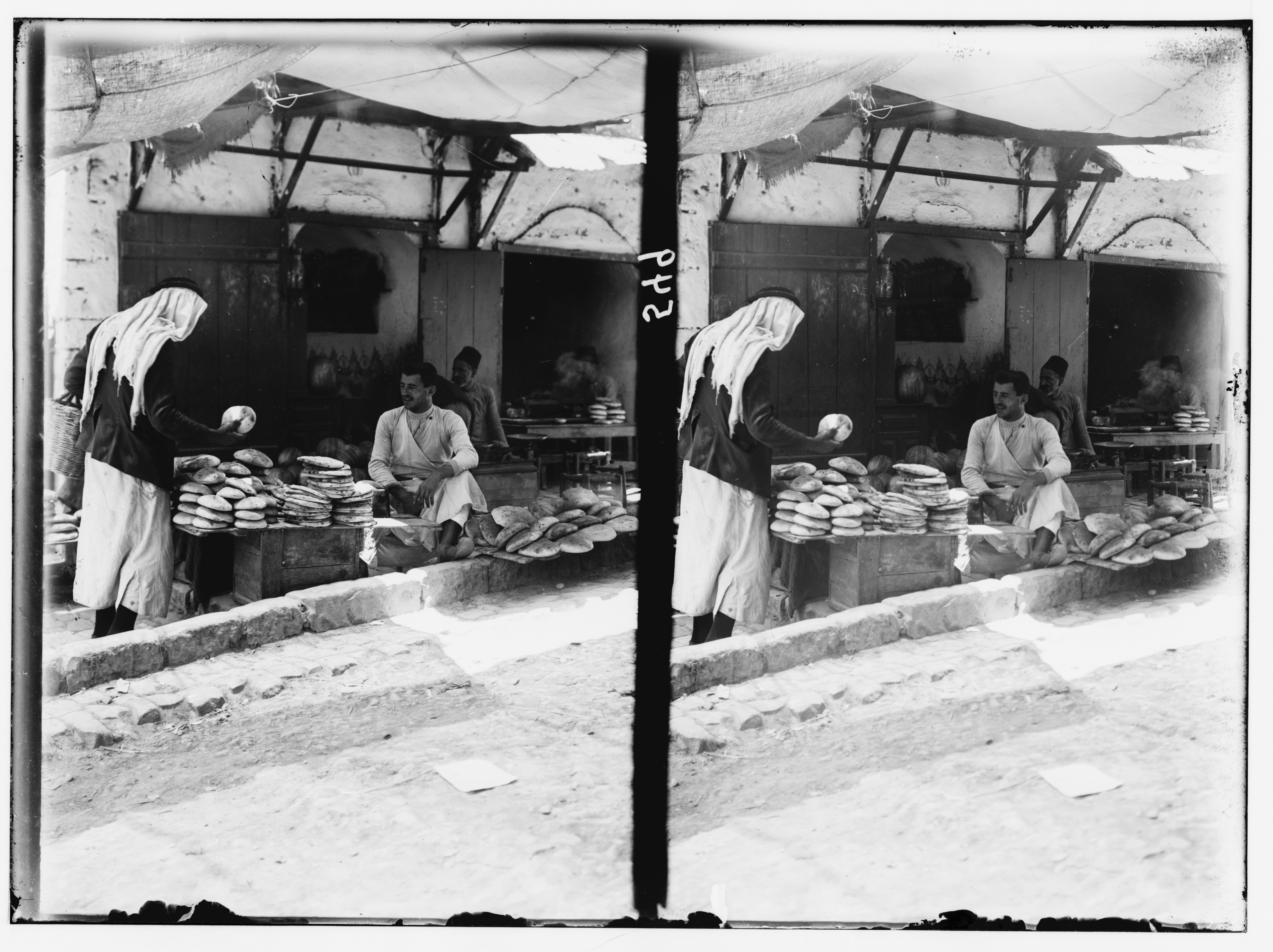 Stereoscopic photograph of a woman and a man standing near a pile of bread in a bakery or market stall.