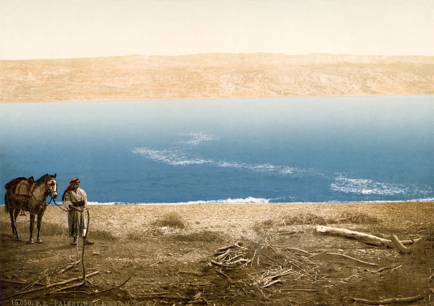 A vintage photograph of a man and a horse standing near the Sea of Galilee, with rolling hills in the background.