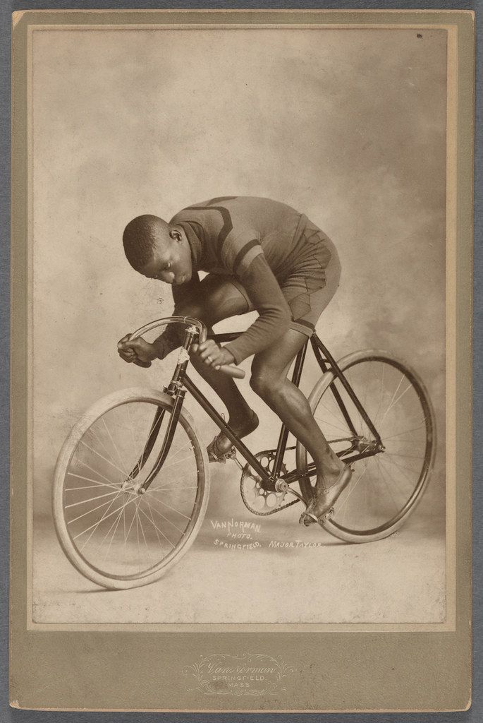 Vintage photograph of a Black man riding a high-wheeler bicycle.