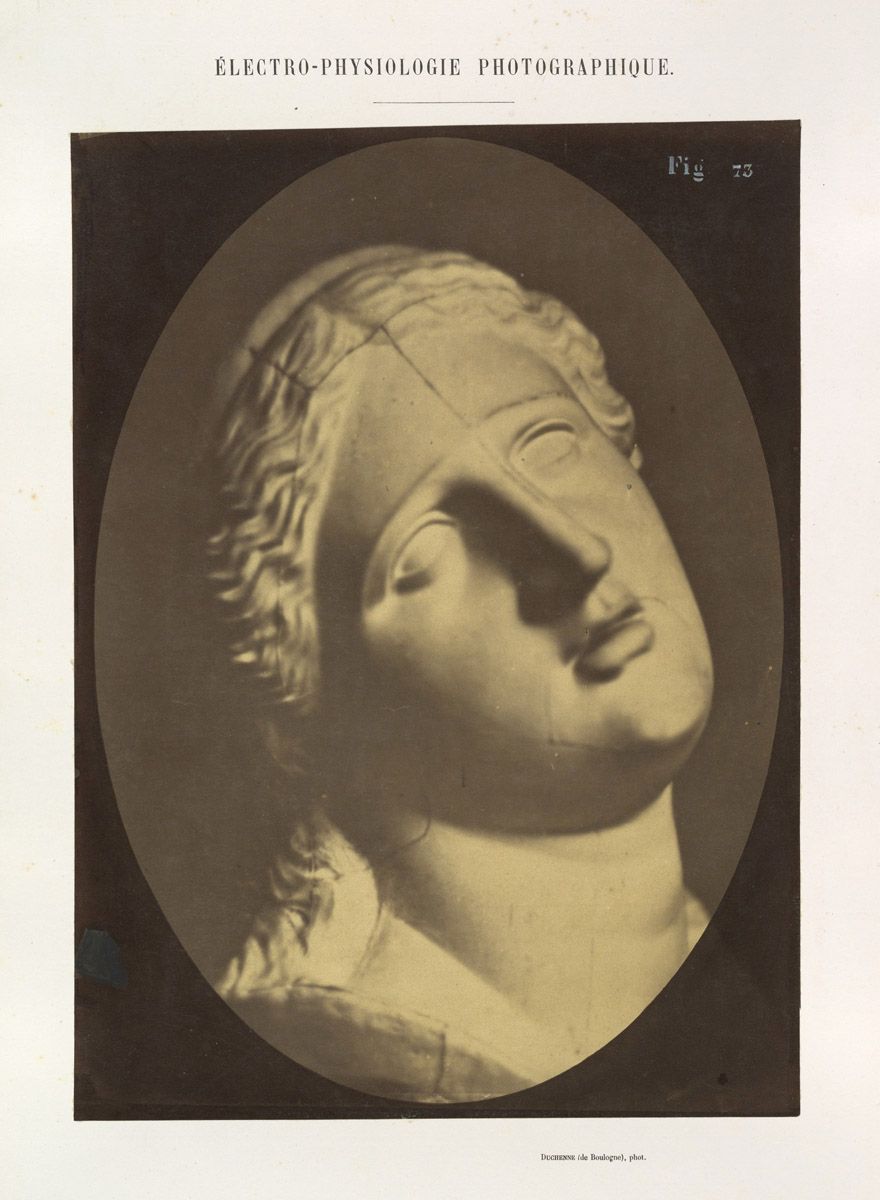 Vintage photograph of a classical bust with a damaged face, presented within an oval frame.