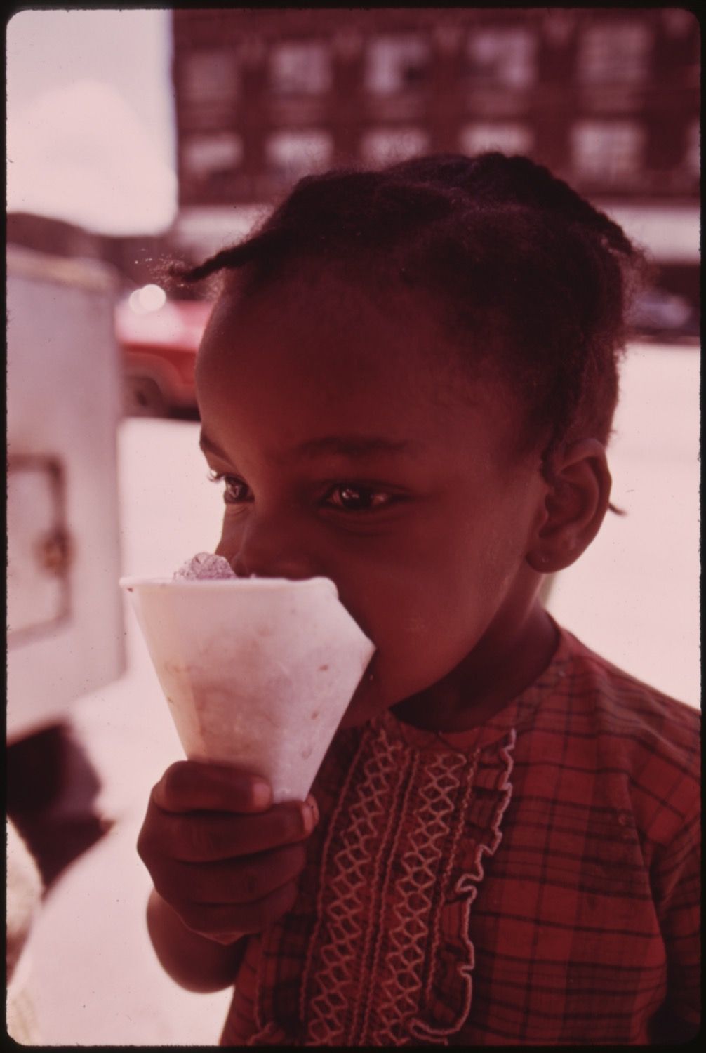 A vintage-style photograph of a young Black child enjoying an ice cream cone on a street.