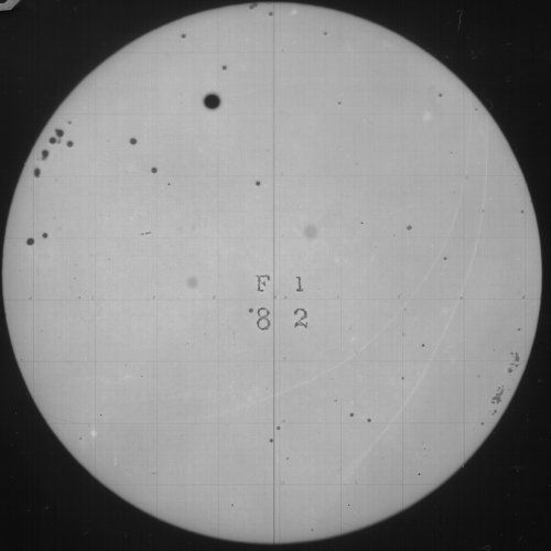 A circular image of the sun with a sunspot and a grid pattern, with handwritten text in the center.