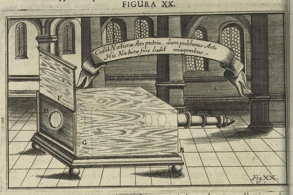A detailed engraving of a bed within a room. The bed is the central focus, appearing as a large, ornate structure with a rectangular base and a raised headboard. It's supported by four cylindrical legs. A curtain is partially drawn around the bed, suggesting privacy or a sense of enclosure. The room itself has a classical architectural style, with arched windows and pillars. The windows are adorned with curtains, and the pillars add to the grandeur of the space. The floor is tiled or paved, and the walls are relatively bare, emphasizing the bed as the focal point. Above the bed, a scroll is displayed with Latin text.