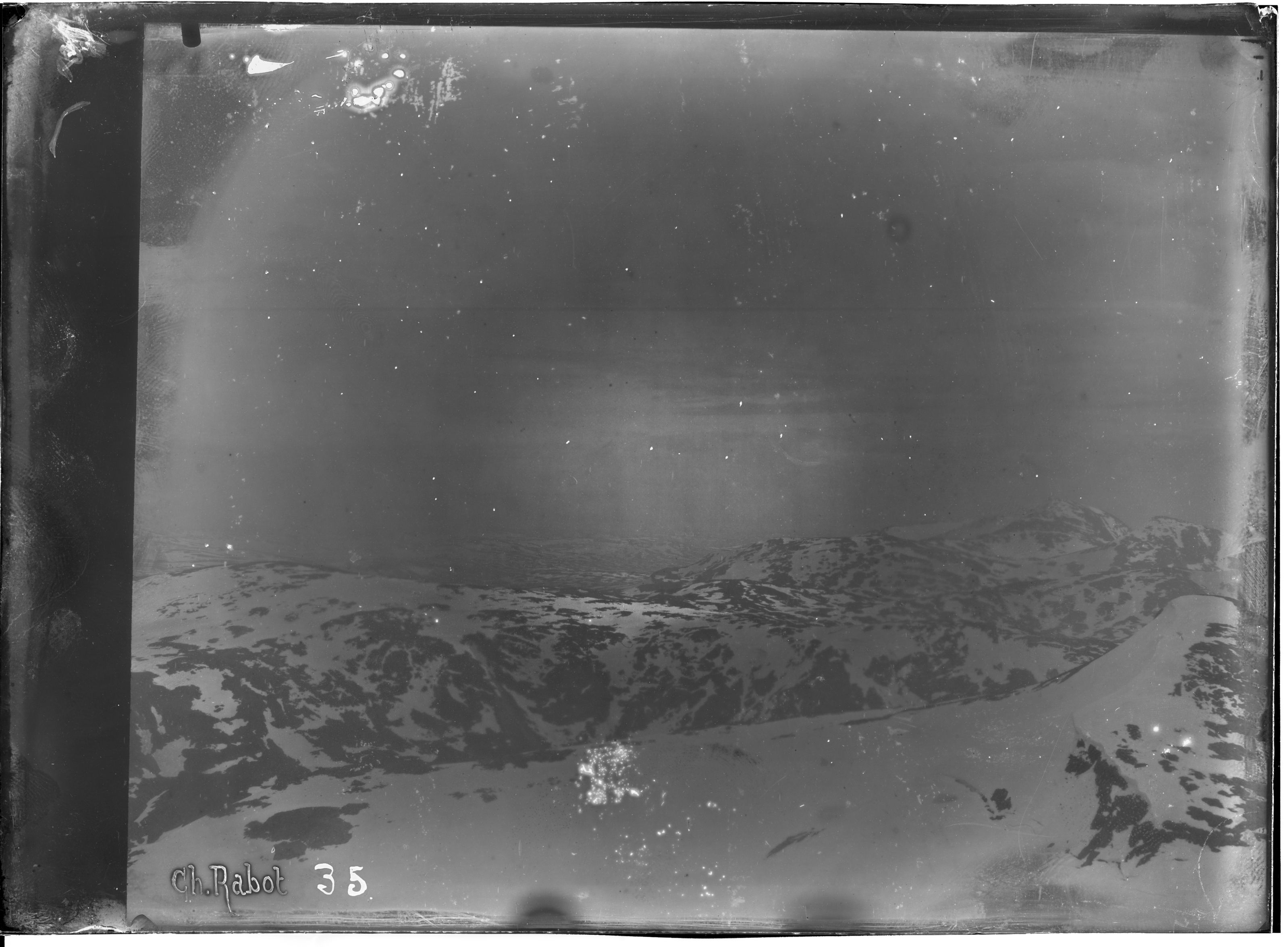 A vintage black and white photograph of a mountain range, captured on a glass plate negative. The mountains are snow-capped and dramatic, with a dark sky above. Handwritten inscription 'Ch. Rabot 35' in the lower left corner.