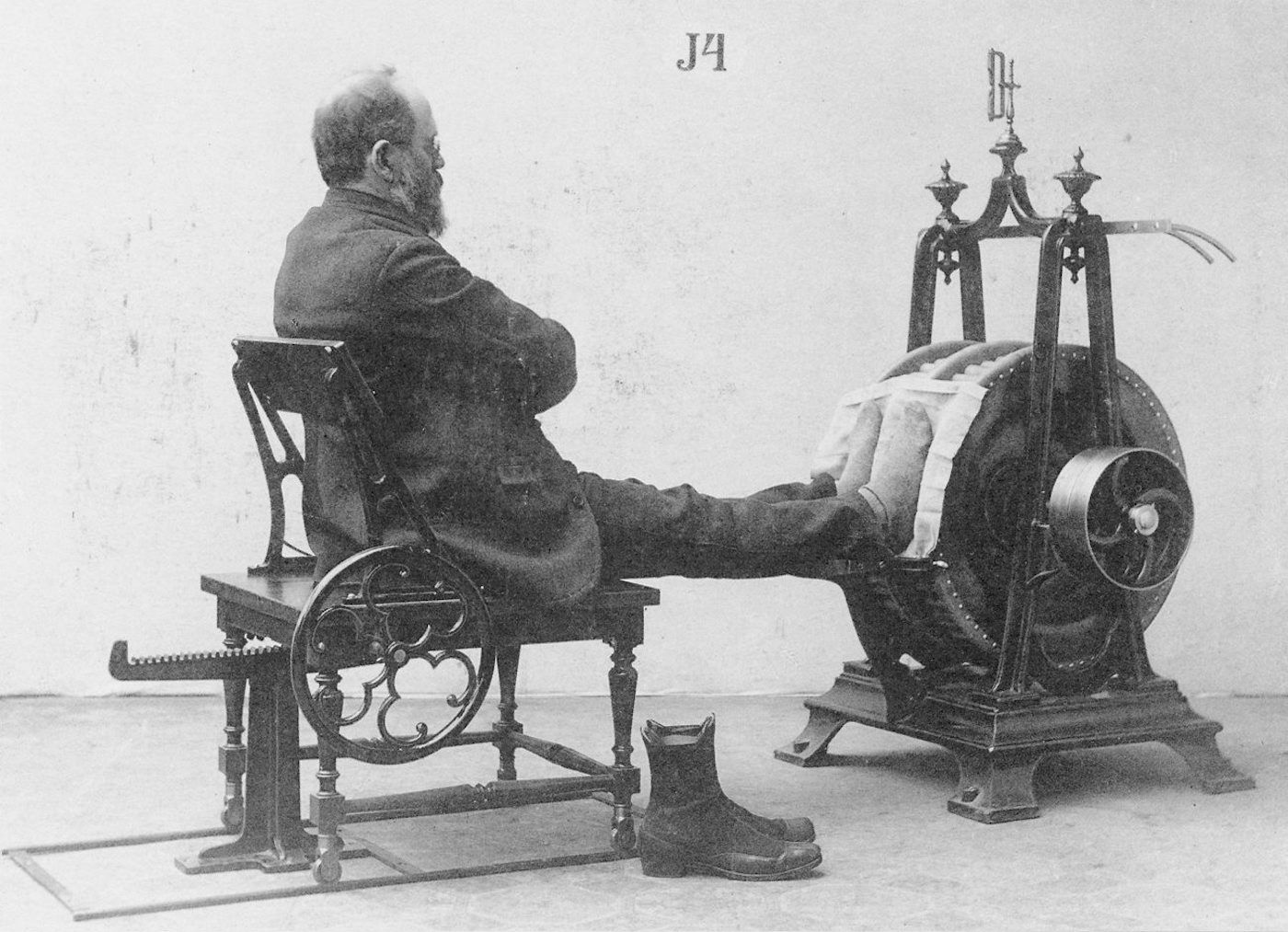 Vintage black and white photograph of a man seated in a complex mechanical chair.